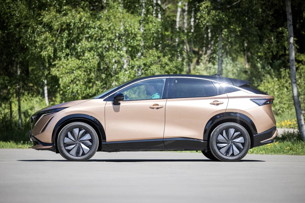 Gullgrå Nissan Ariya foran grrønne trær